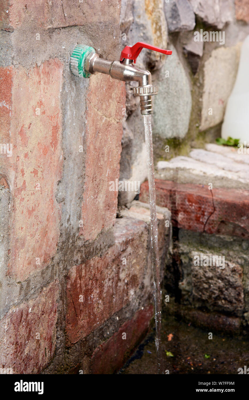 Faucet in a brick wall and running water Stock Photo