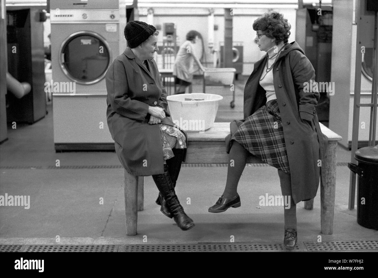 Public Laundry 1970s UK. Women taking their dirty used clothes to a public  laundry to get them washed. Woman chatting with friend while waiting for  their clothes washing to finish. Battersea south