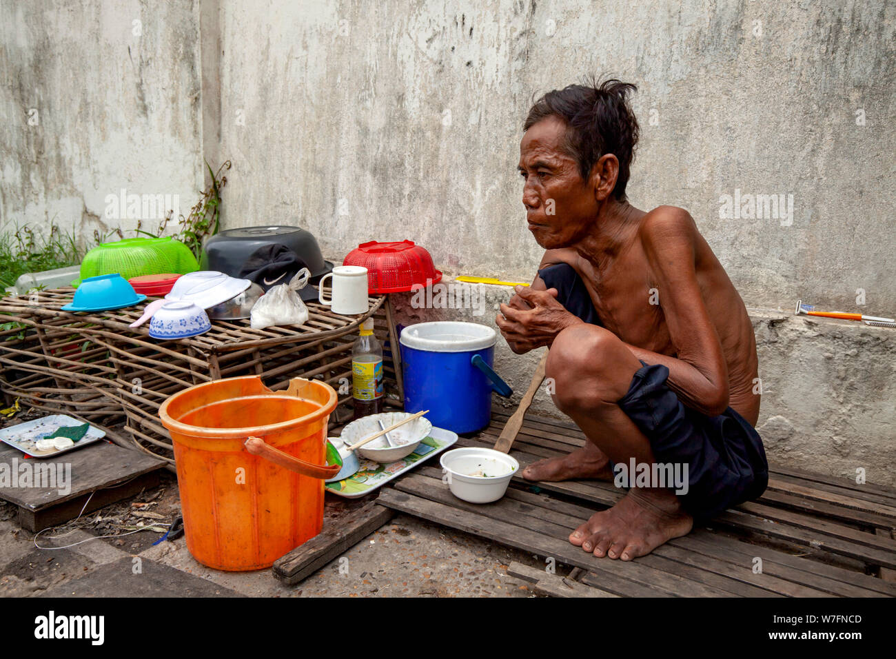An elderly homeless Cambodian man sits near his ramshackle home on a city street in Kampong Cham, Cambodia. Stock Photo