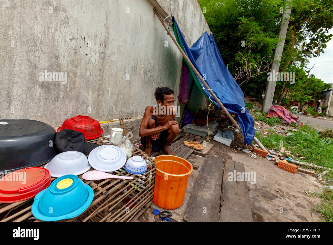 An elderly homeless Cambodian man sits near his ramshackle home on a city street in Kampong Cham, Cambodia. Stock Photo