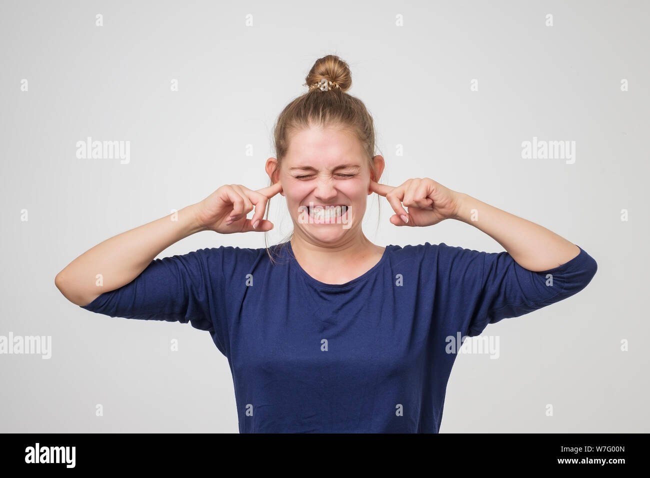 Young woman covering her ears with hands not wanting to hear too loud sound. Pretty girl trying to protect herself from noise Stock Photo