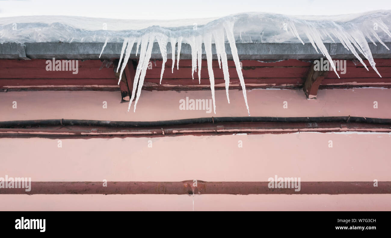 Icicles hang on the roof over pink urban wall Stock Photo