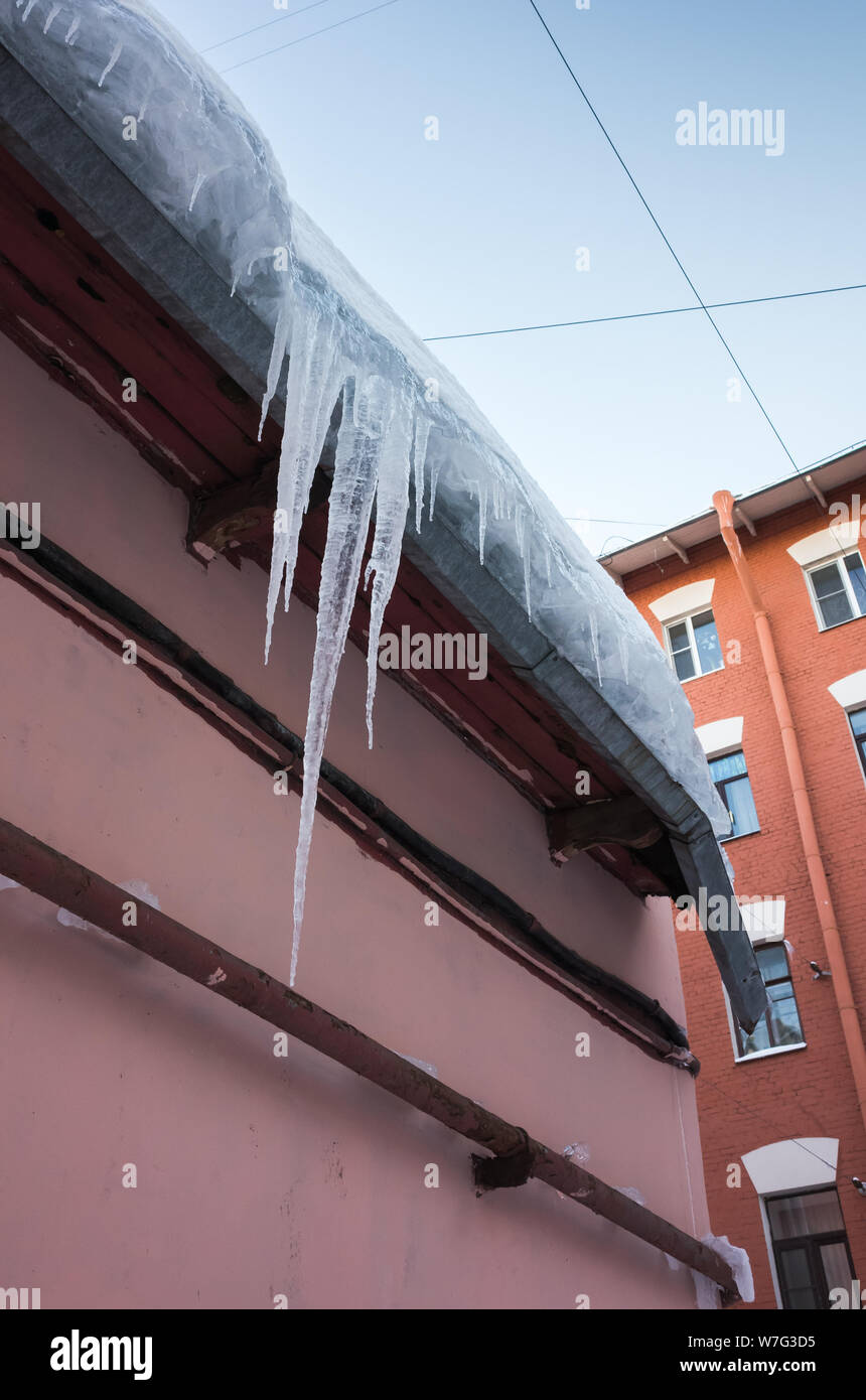 Icicles hang on the roof of pink urban building in Saint-Petersburg; Russia. Vertical photo Stock Photo