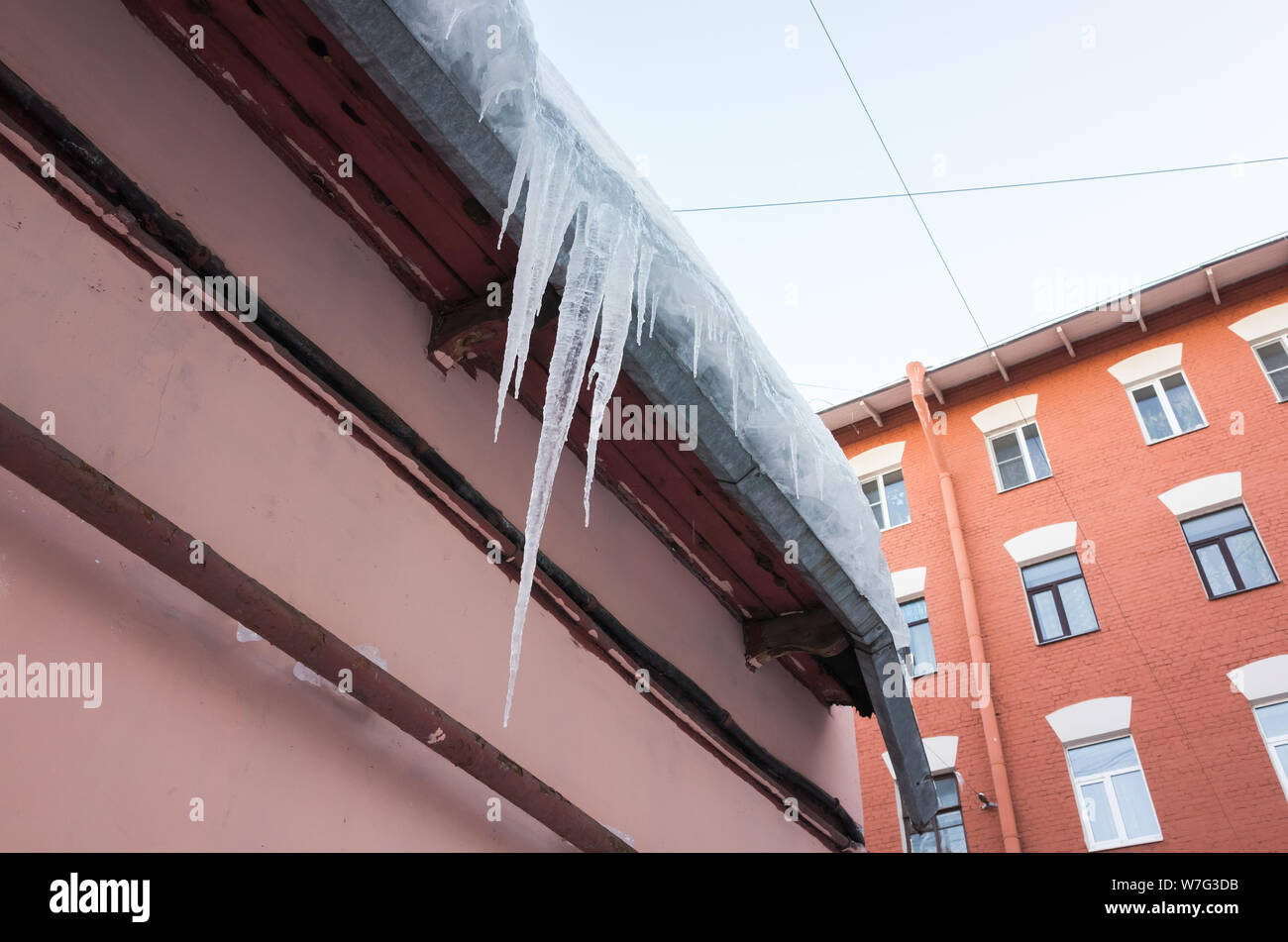 Icicles hang on the roof of pink urban building, Saint-Petersburg, Russia Stock Photo