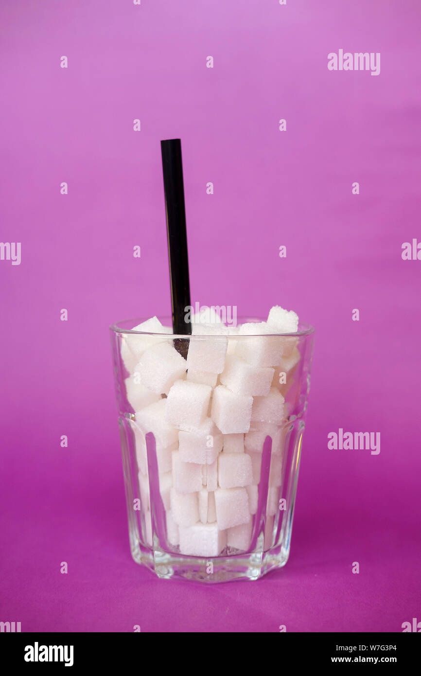 Glass full of sugar cubes  on purple background. Diabetes, sugar disease, unhealthy food, diet concept. Copy space Stock Photo