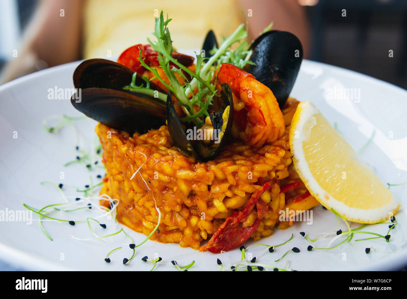 Spanish paella with mussels and shrimps decorated with lemon and arugula. Served on a white plate with lemon. Closeup fo a beautiful rice dish. Stock Photo
