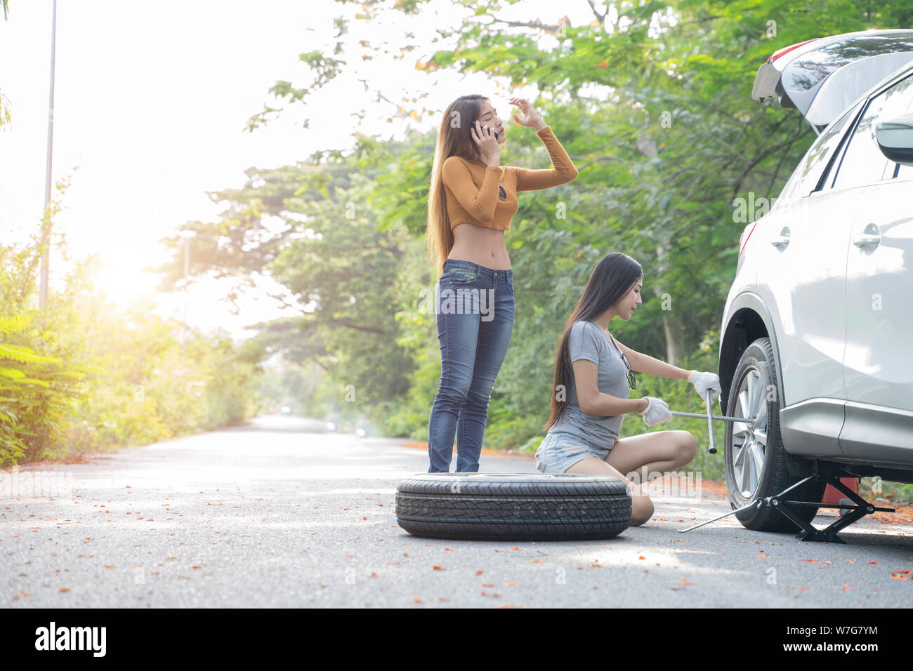 Female driver changing tyre on her broken car  and her friend is calling for help. Stock Photo