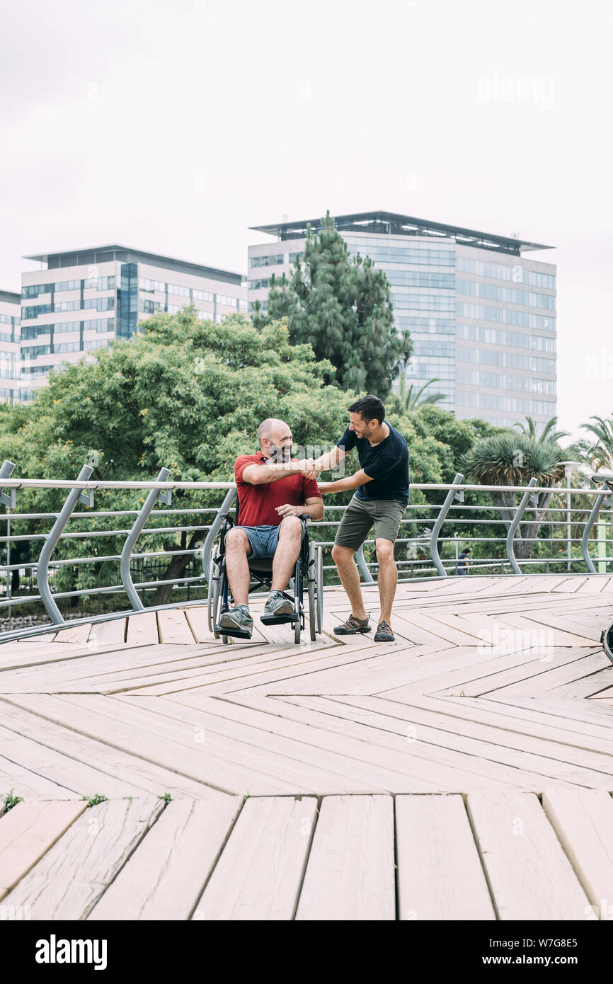 disabled man in wheelchair shake hands with his friend during a walk at ...