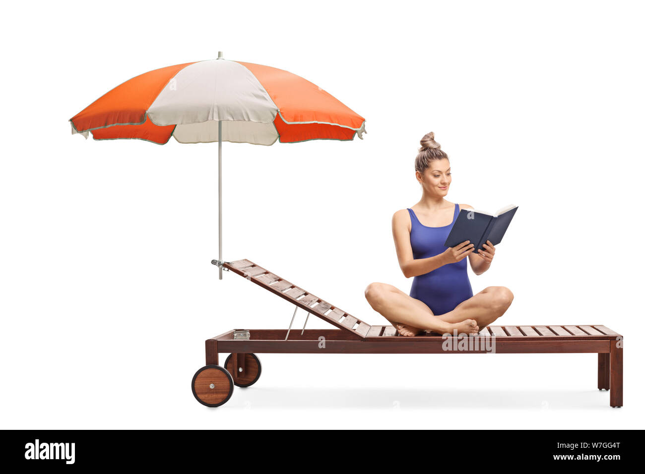 Young woman in a swimming suit sitting on a sunbed with umbrella and reading a book isolated on white background Stock Photo