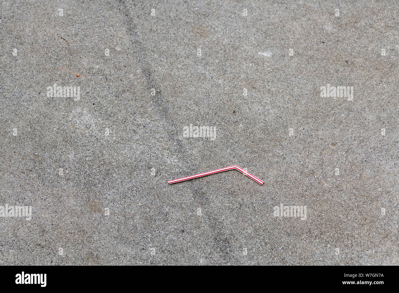 Plastic drinking straw discarded on cement paving surface in urban area. Metaphor plastic straw pollution, environmental pollution, plastic straw ban. Stock Photo