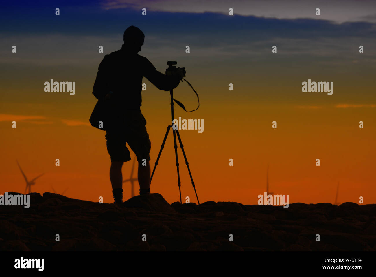 A photographer in silhouette using a DSLR camera and tripod taking a ...