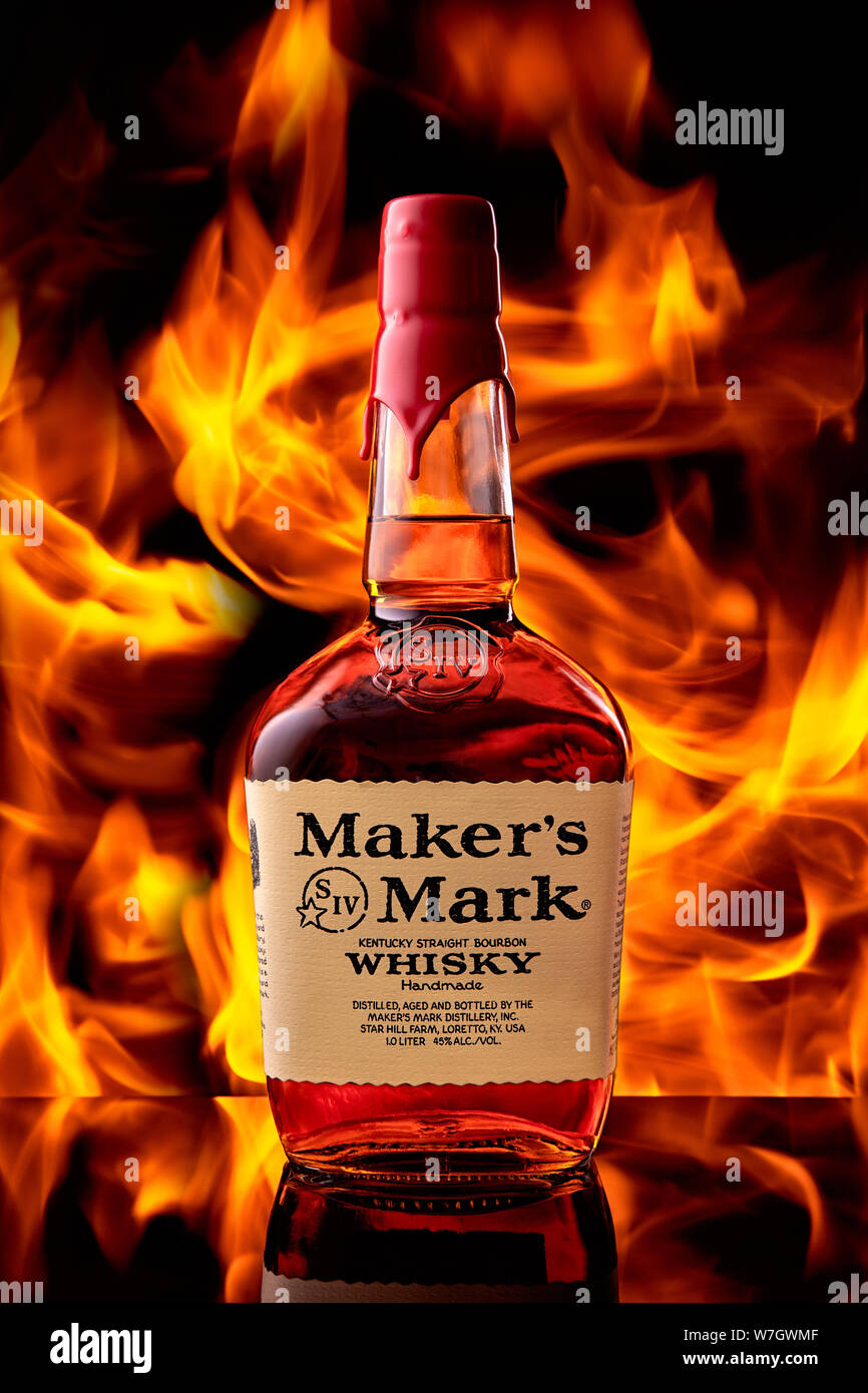 A bottle of Maker's Mark whiskey stands on a glass bar top against the background of a fire