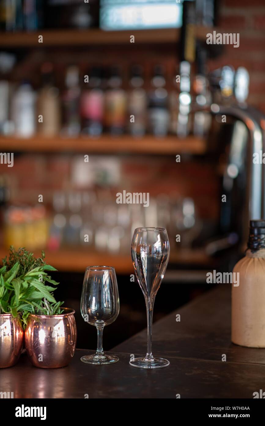 Vertical shot of two tall glasses on a wooden surface and a blurred background at a bar Stock Photo