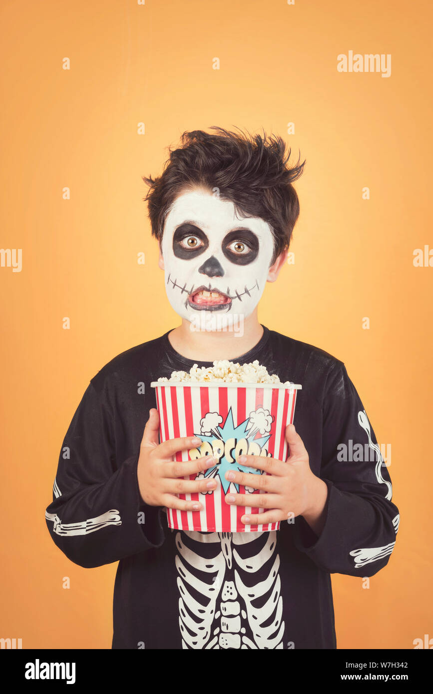 Happy Halloween.funny child in a skeleton costume with popcorn against orange background Stock Photo