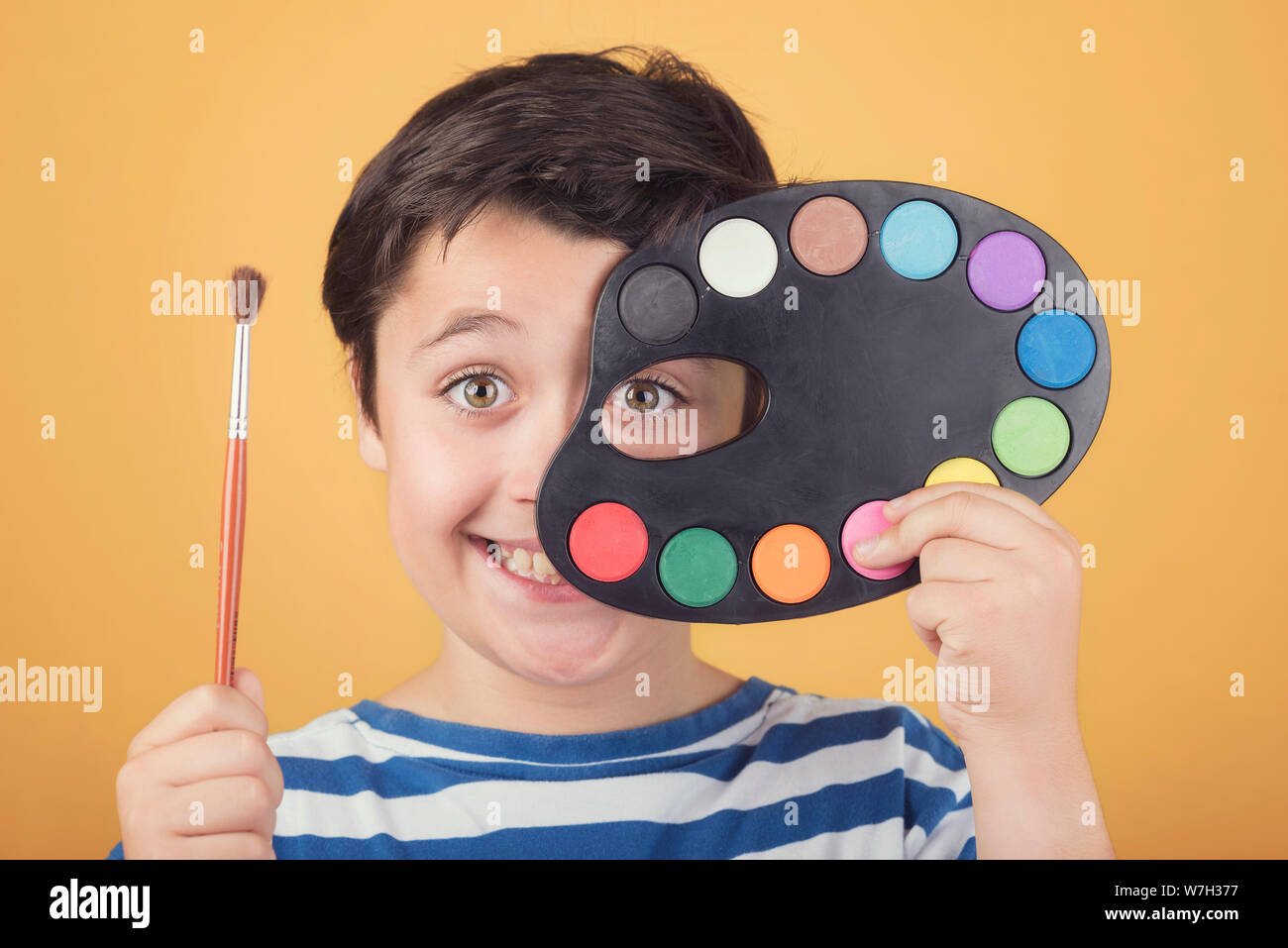 Portrait of child with colorful palette against yellow background Stock Photo