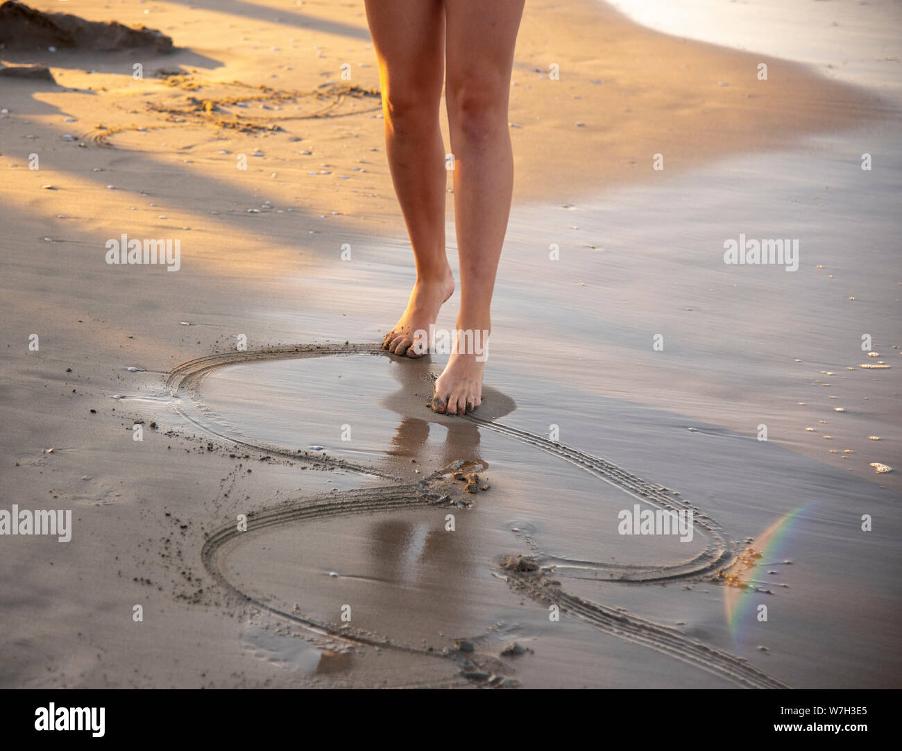Female bare feet draw patterns on the sea sand. Shells are visible on ...