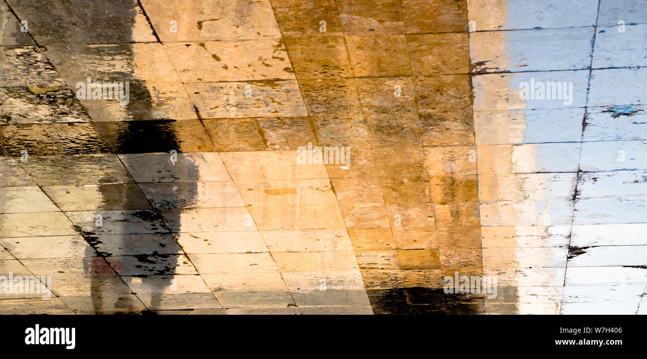 Blurry reflection shadow silhouettes of  a woman and a child walking on a wet street  on a sunny summer day on old town stone pavement Stock Photo