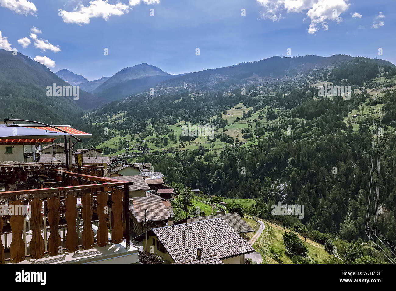 Terrace of a rustic cafe in the Swiss Alps overlooking wooded mountains against a blue sky. Stock Photo