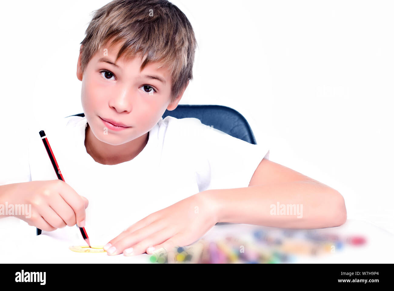 Young kid sitting at the desk, drawing with a pen, on white background