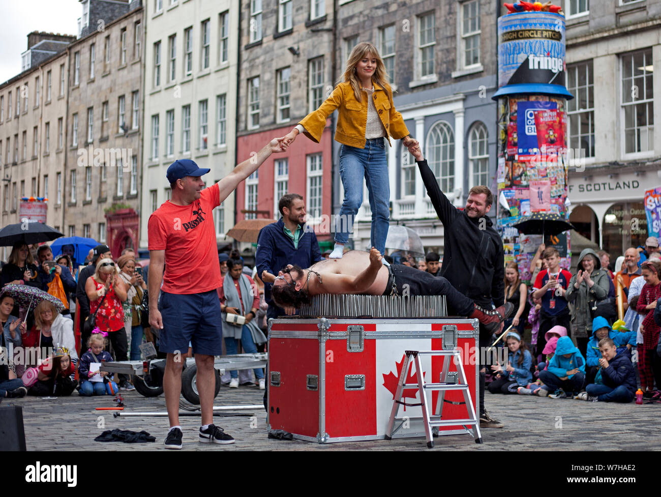 Royal Mile, Edinburgh, Scotland, UK. 6th August 2019. Stickman, Canadian Street Performer at  Edinburgh Festival Fringe for his 39th year in succession once again enthralls the audience with  his dangerous tricks, juggling a garden fork, sharp spear above volunteer, and his finale lying on a bed of nails with an attractive lady standing on his stomach. Stock Photo