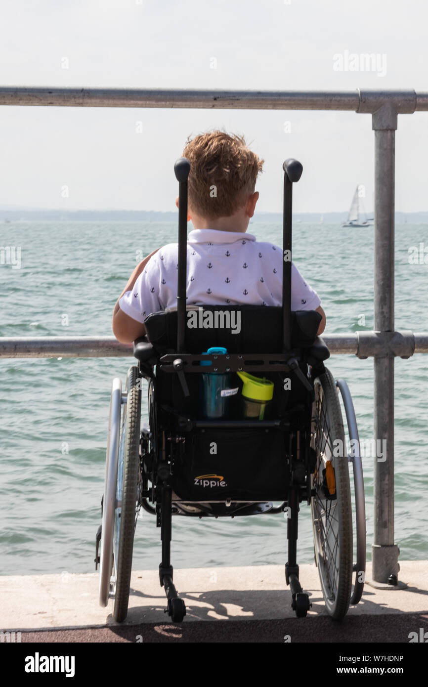 A small boy in a wheelchair at the seaside looking at the view of the sea Stock Photo