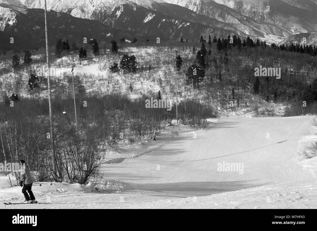 Skier downhill on snowy ski slope at sun winter day. Caucasus Mountains. Hatsvali, Svaneti region of Georgia. Black and white retro toned landscape. Stock Photo