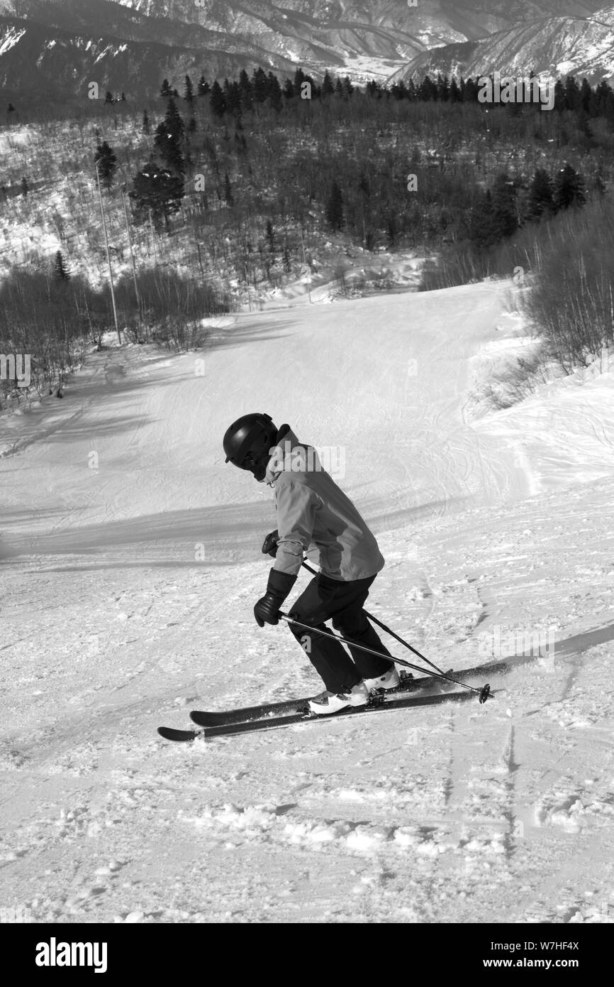 Skier descent on snowy ski slope at sun winter day. Caucasus Mountains. Hatsvali, Svaneti region of Georgia. Black and white toned image. Stock Photo
