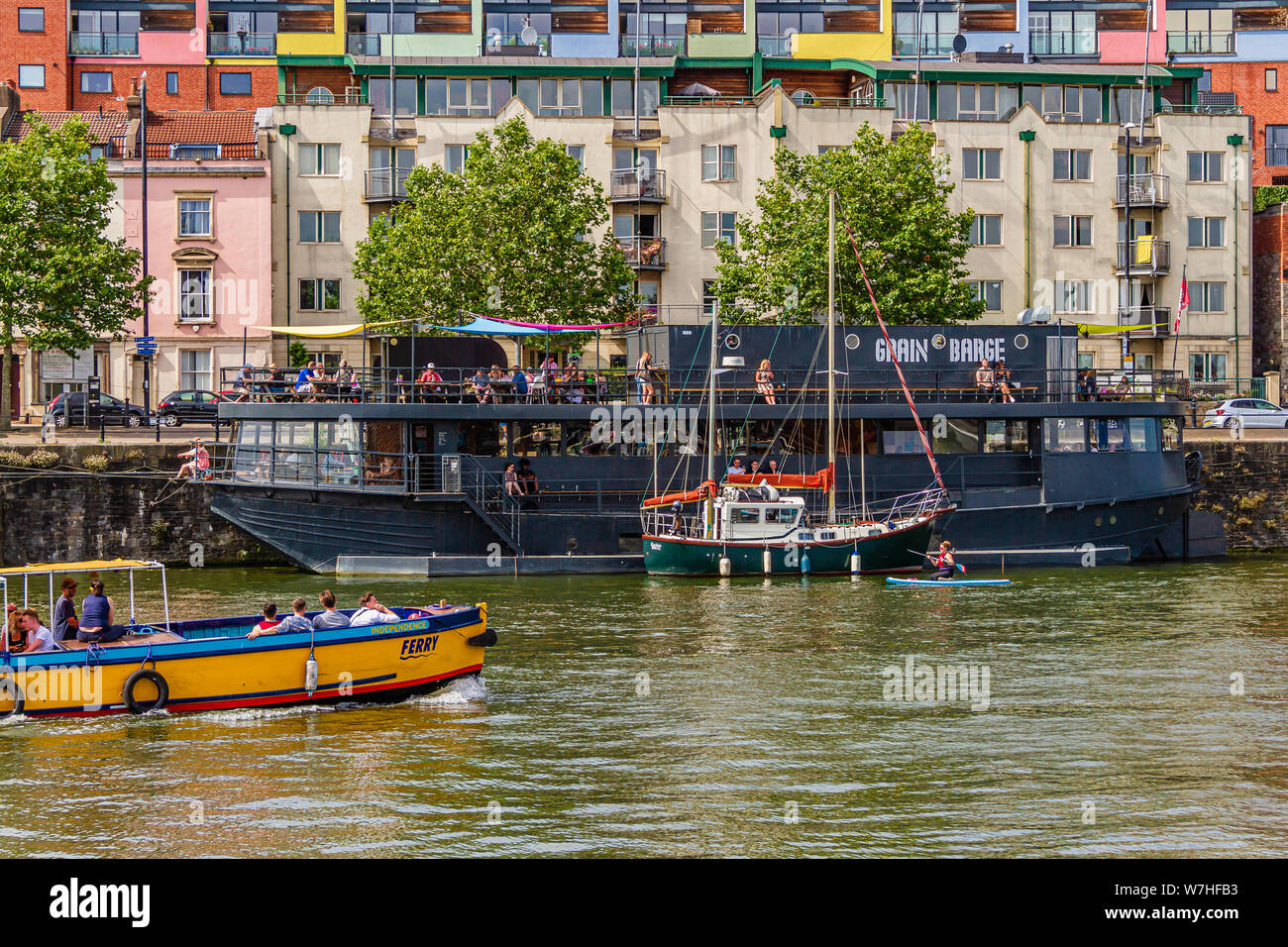 A ferry passing the Grain Barge, a bar in a converted barge and owned by Bristol Beer Factory. Mardyke Wharf, Hotwells, Bristol, UK. July 2019. Stock Photo