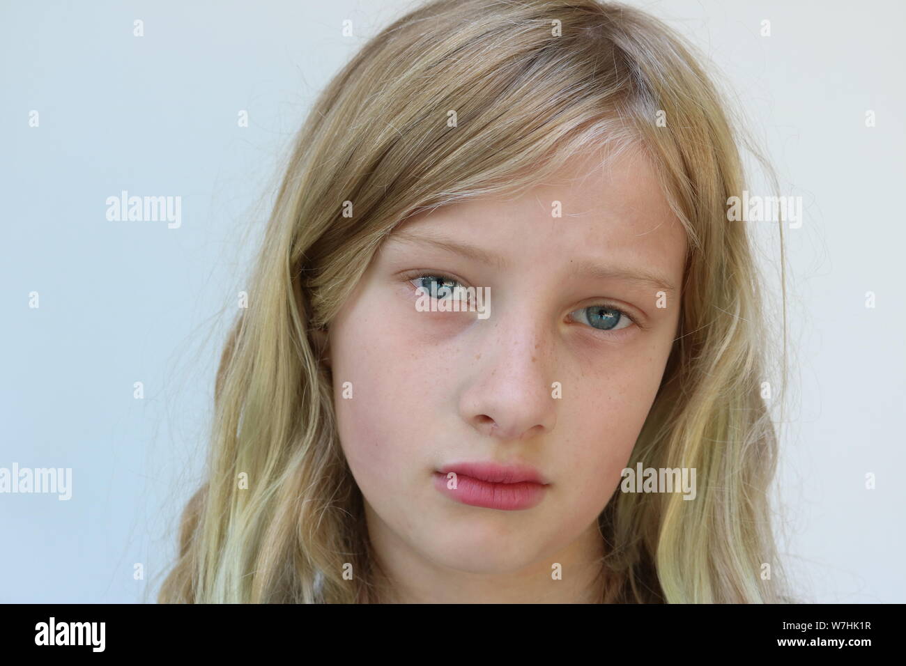 Portrait of a beautiful blond preteen heartbroken girl against a white background Stock Photo