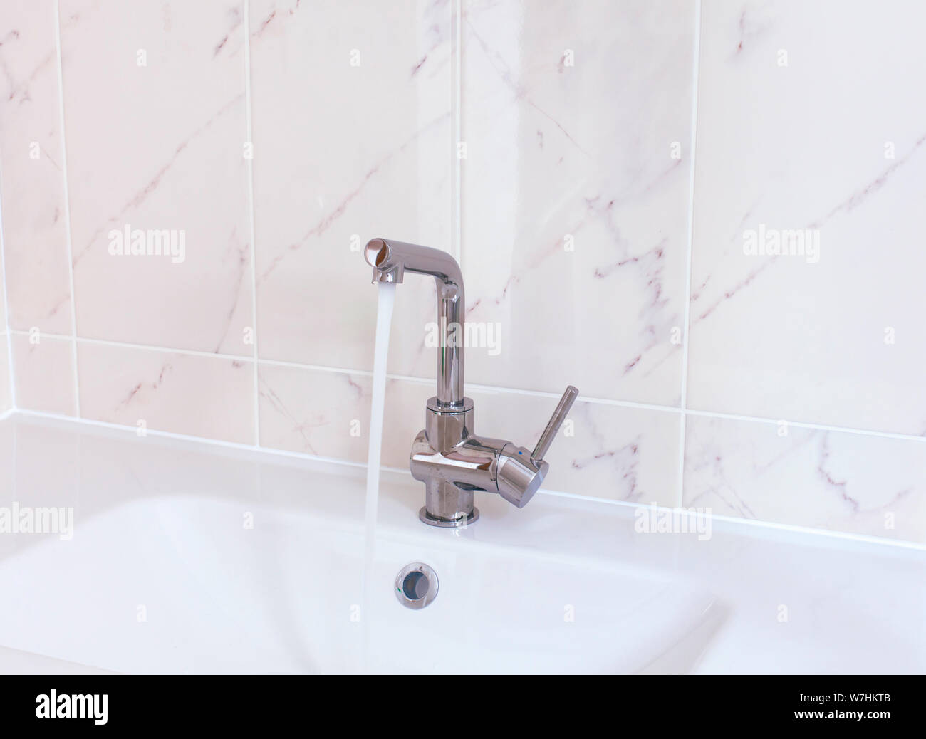 Faucet pouring water into white sink in domestic bathroom. Closeup. Stock Photo