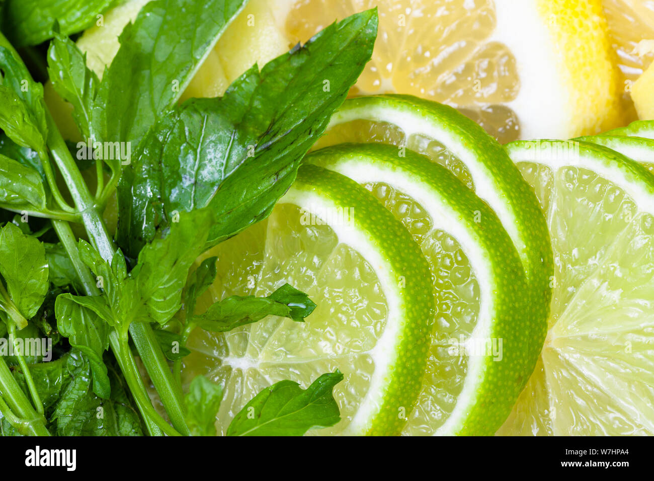 food background - cocktail ingredients, green mint leaves and thin sliced fresh limes, lemons, ginger close up Stock Photo