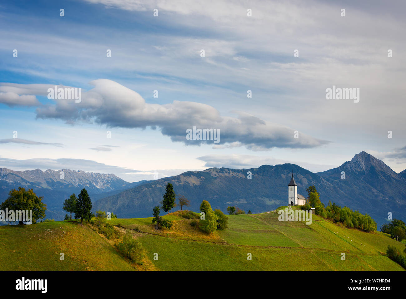 The church of St. Primus on the top of a hill in a landscape with the Kamnik Alps in the background under strange clouds in Jamnik, Kranj, Slovenia. Stock Photo