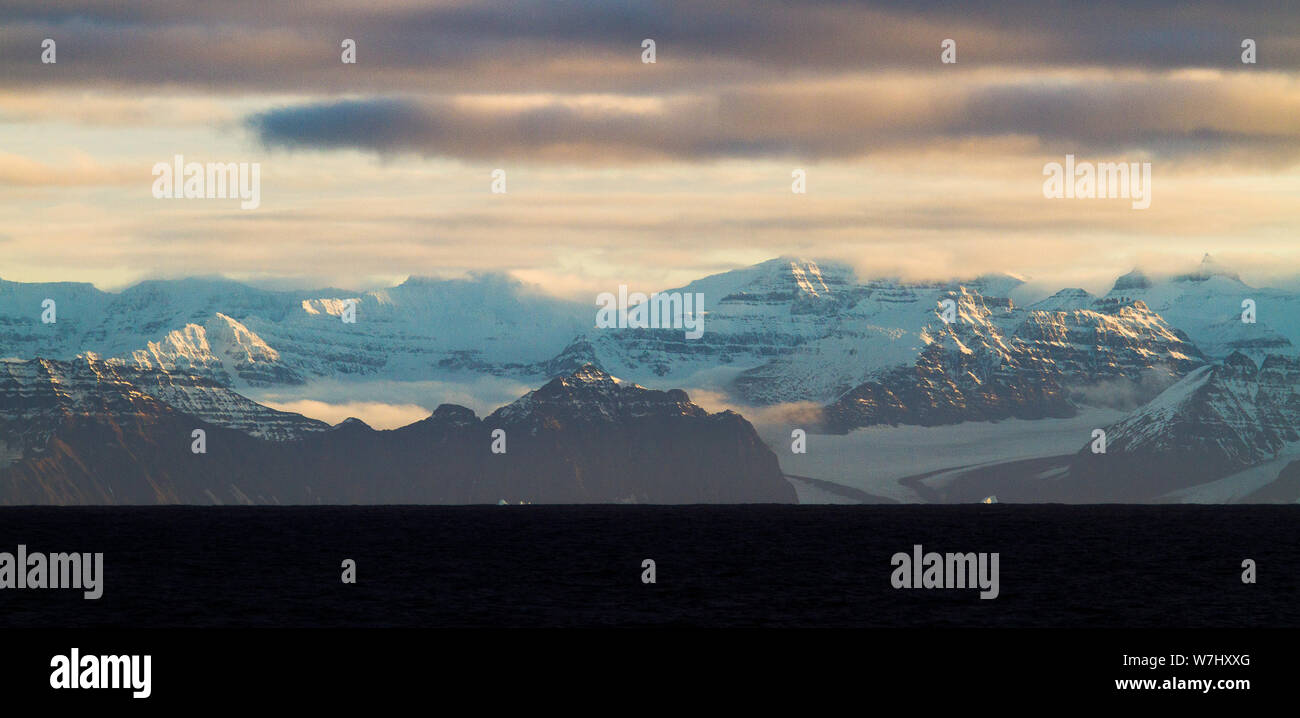Mountain ranges emerge with scratched nails marks from the glowering ocean and sky in Scoresby Sund, eastern Greenland Stock Photo