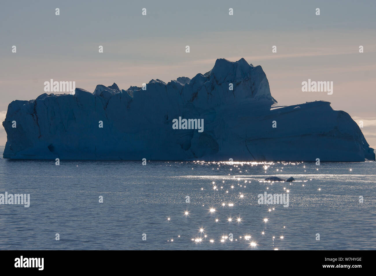 Dazzling lights dance on the shallow waves in front of a massive iceberg in the bay around Sydkap, Greenland. Stock Photo