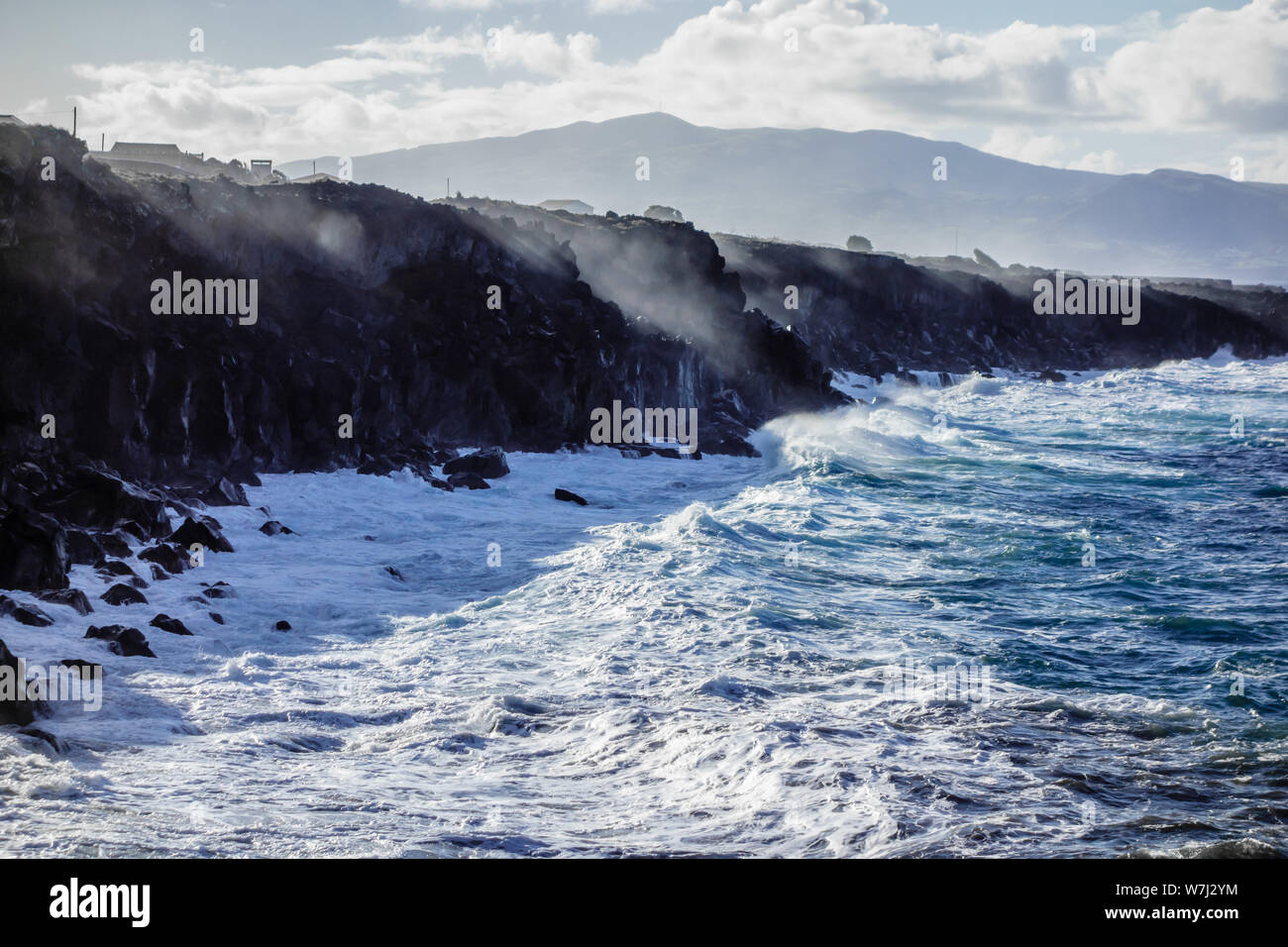 Ocean waves splashing on jagged cliffs with spray reflecting sunlight, in Azores, Portugal. Stock Photo