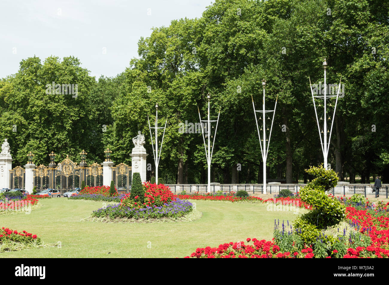 Landscape view of grass and gardens full of flowers near Buckingham palace and gates on a sunny day.  Tourists and policeman nearby Stock Photo