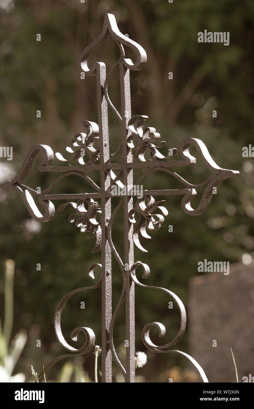 Old wrought iron cross next to the grave. Green background with blurred