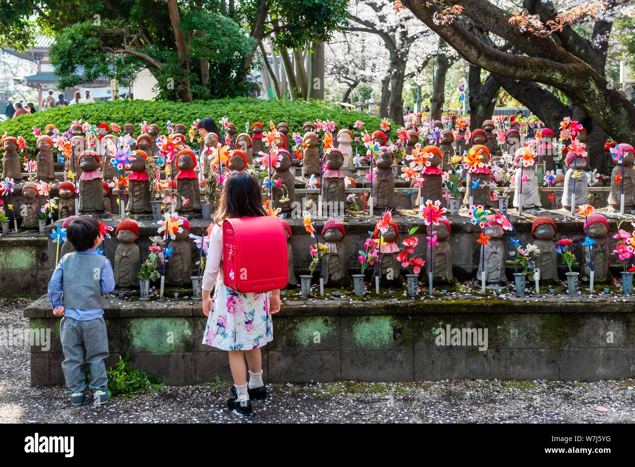 Two schoolchildren in front of Jizo statues with red caps, protective deities for deceased children, Unborn Children Garden. Zojoji Temple Stock Photo