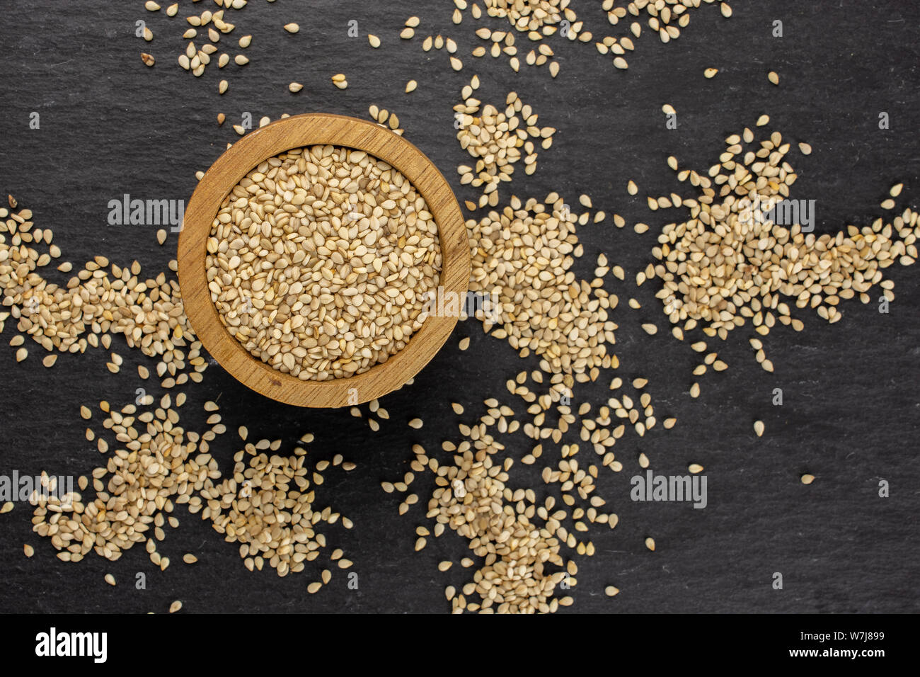 Lot of whole unpeeled sesame seeds in wooden bowl flatlay on grey stone