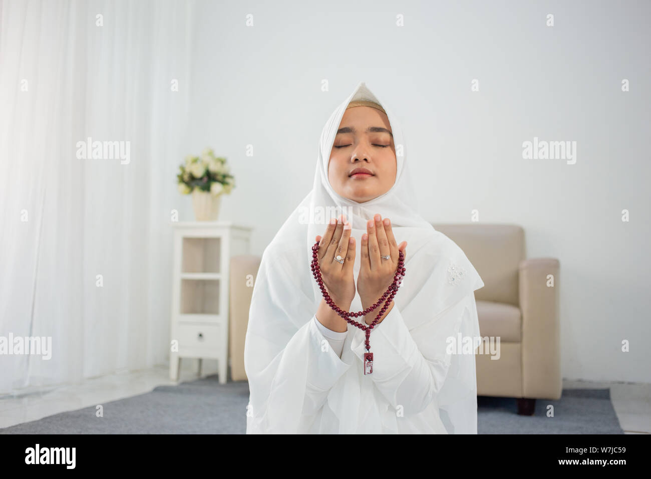 Muslim young woman praying in white traditional clothes Stock Photo