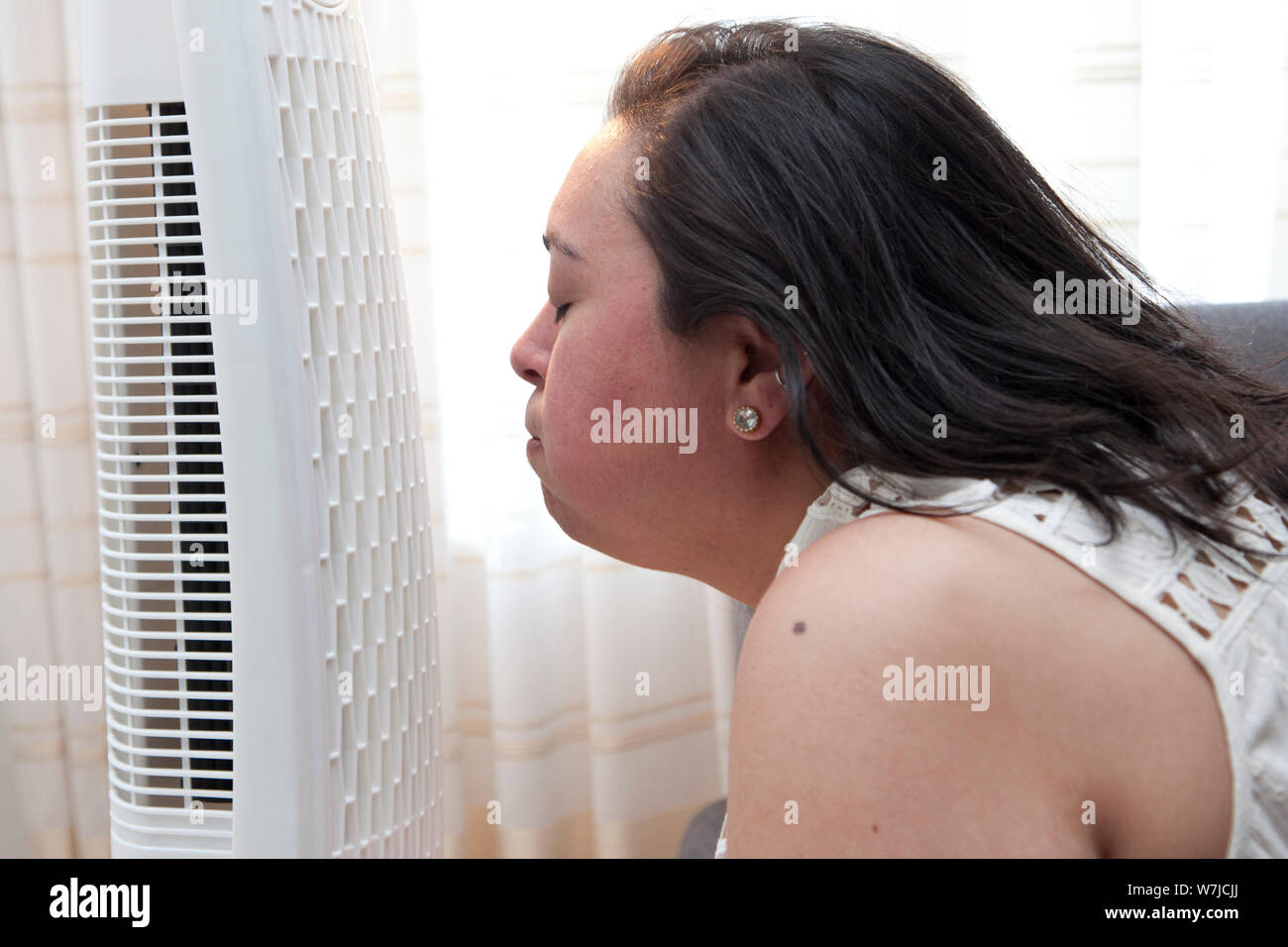 Woman enjoys the cool breeze of a fan at home in the heat Stock Photo