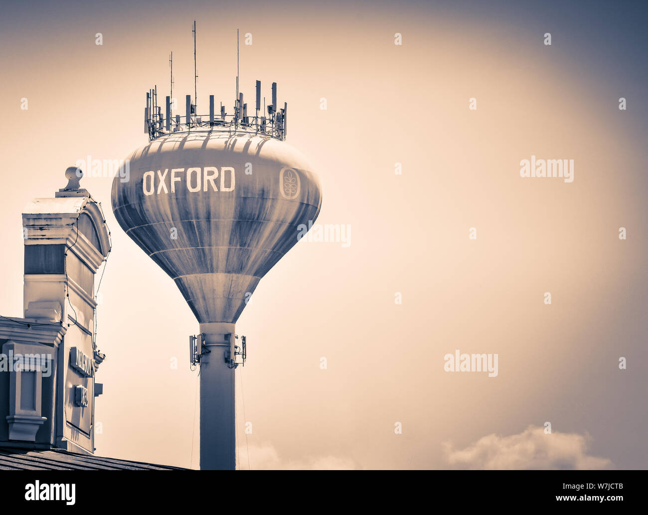 A water tower with Oxford painted on it with cell phone communication systems on top above the town square in downtown Oxford, MS, in sepia Stock Photo