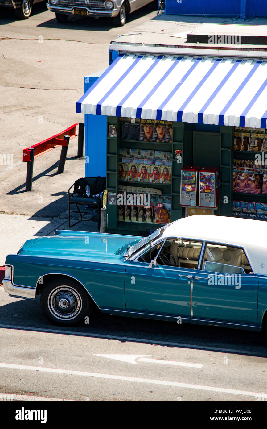 Classic blue luxury vehicle, parked before a magazine stand on a busy Los Angeles street on a sunny summer day. Stock Photo