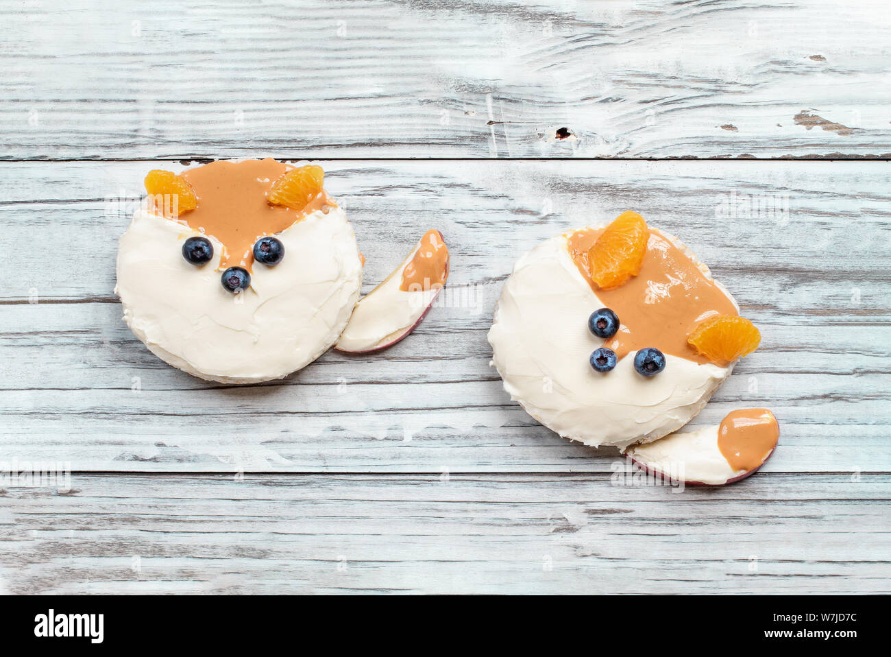 Fun food for kids. Rice cakes in the shape of foxes lying on a rustic white table. Fox is made from cream cheese, peanut butter, apple slices, oranges Stock Photo