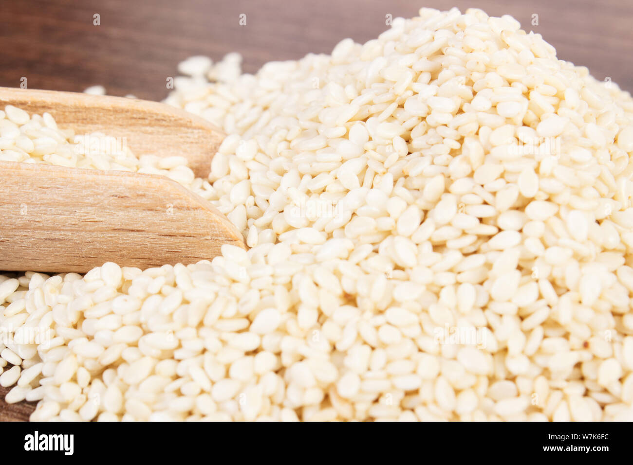 Heap of sesame seeds with wooden scoop on board, concept of healthy