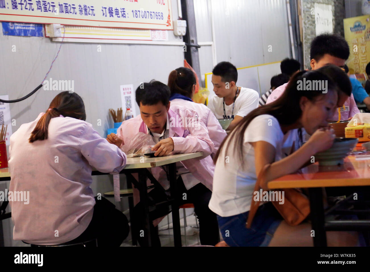 Chinese workers eat meals at a roadside restaurant after leaving work outside the Pegatron Changshuo factory for the assembly of Apple's iPhone and ot Stock Photo