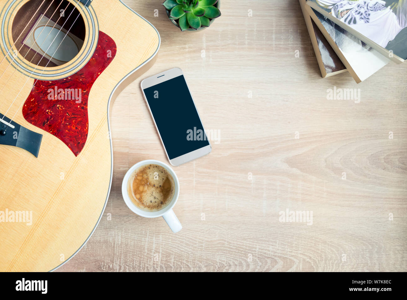 Top view of cosy home scene. Guitar, books, cup of coffee, phone and succulent plants over wooden background. Copy space, mock-up. Stock Photo