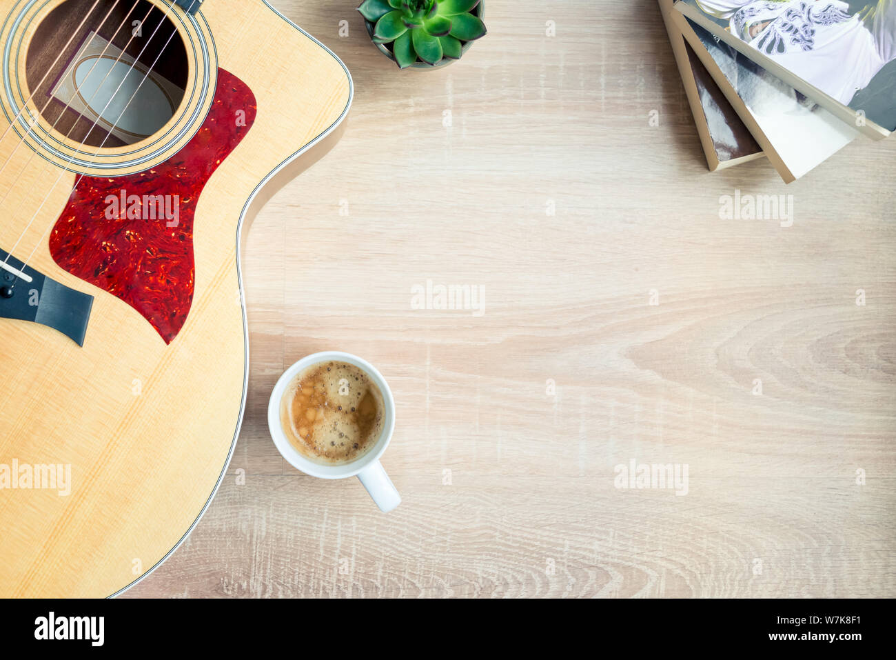 Top view of cosy home scene. Guitar, books, cup of coffee and succulent plants over wooden background. Copy space. Stock Photo