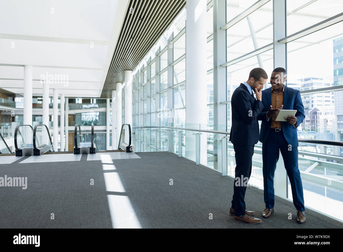 Two businessmen stand using tablet in office lobby Stock Photo