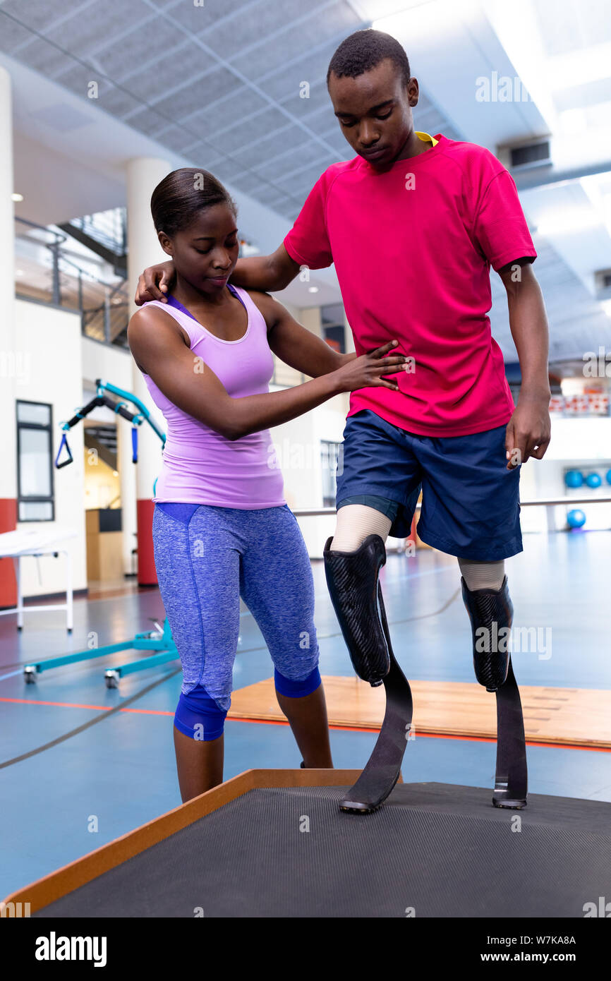 Female physiotherapist helping disabled man walk with prosthetic leg on ...